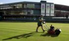 A member of the Wimbledon groundstaff mows an outside court in front of number one court at Wimbledon.