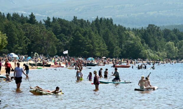 Loch Morlich busy during the heatwave with people in water and on sand.