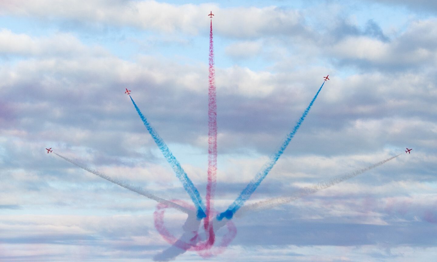 Five Red Arrows plane shoot out from a central point with blue and red smoke. 