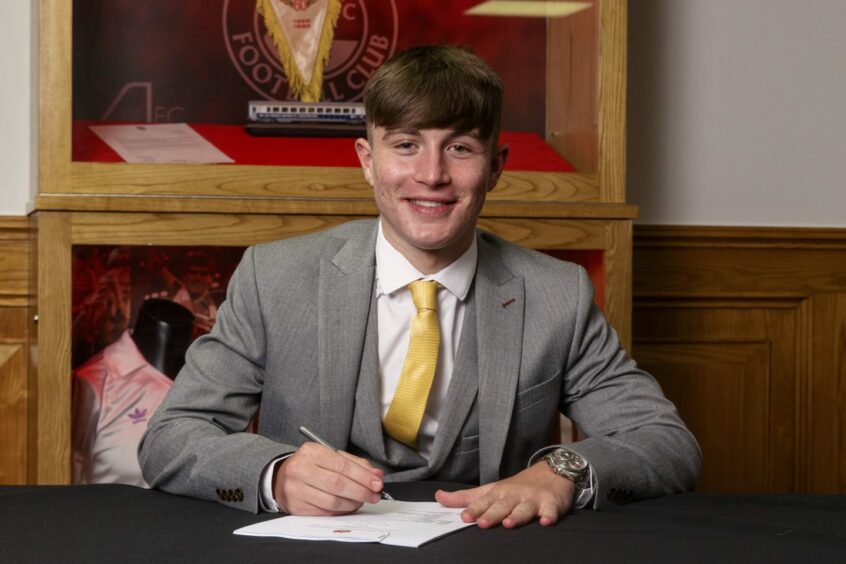 Alfie Bavidge smiling while signing his full-time contract with the Dons.