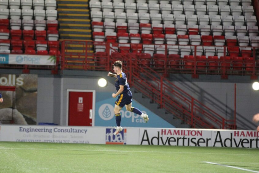 Aberdeen striker Alfie Bavidge in mid-air while celebrating on the pitch.