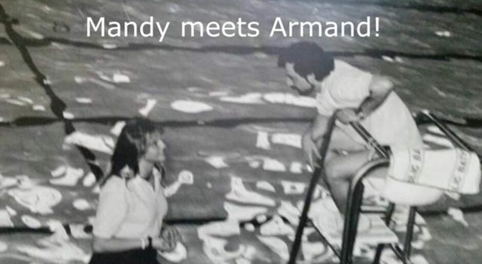 A black and white still from the film, of Mandy and Armand Sangbarani. Armand leans down from his lifeguard chair while Mandy stands to the left.