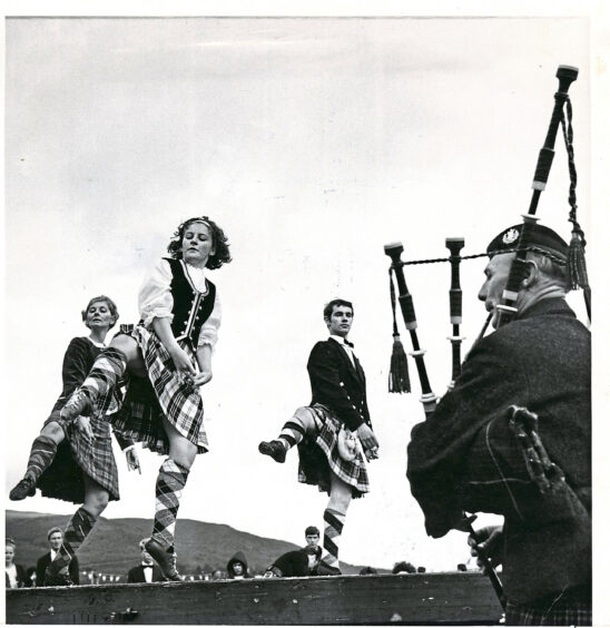 Highland dancers doing their routine in front of a piper playing at the Ballater Highland games
