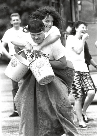A man with a woman on his back inside a sack carrying buckets of water