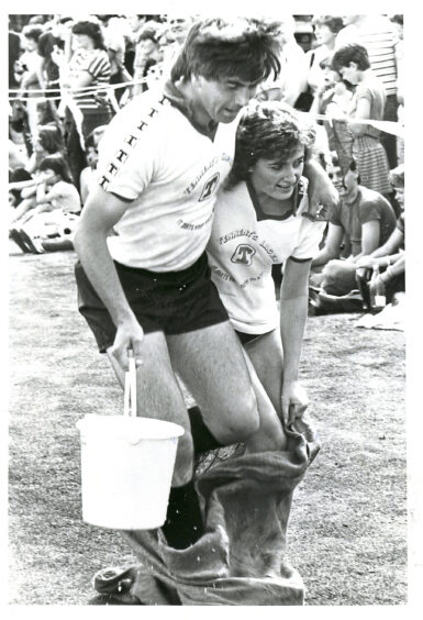 A man and woman hopping in a sack and holding a bucket of water
