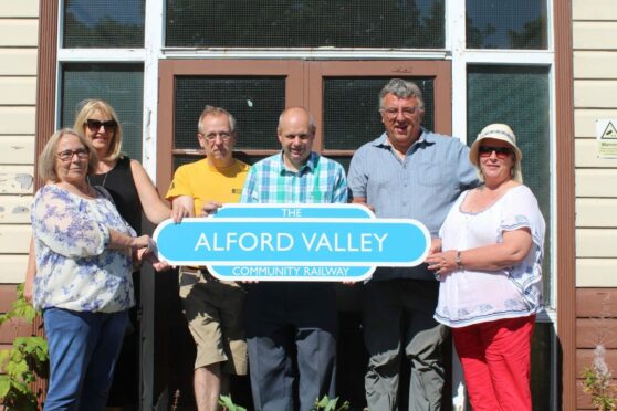 Alford Valley Community Railway board members stand at the station building with the new sign