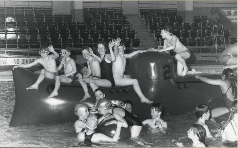 A black and white image of children playing on an inflatable submarine in the Bon Accord Baths. 