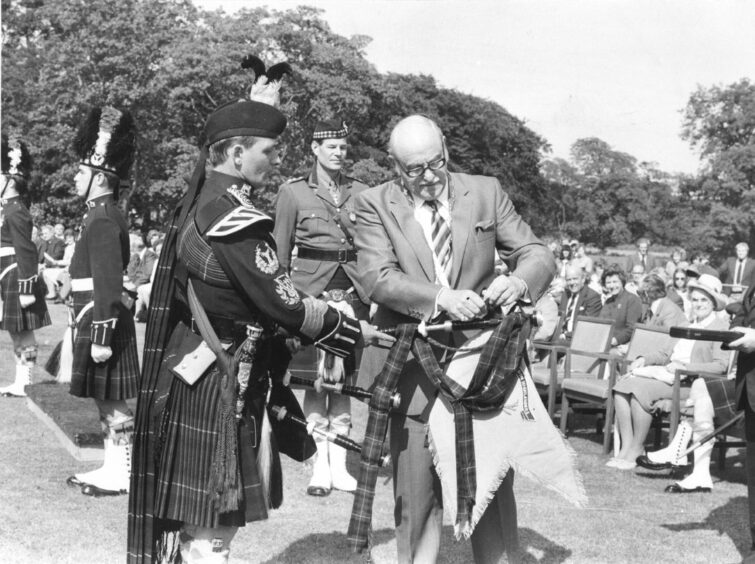 1980 - Convener of Grampian Regional Council, Councillor Sandy Mutch, attaches a banner to the bagpipes of Pipe Maj. Ronald Henderson from Huntly.