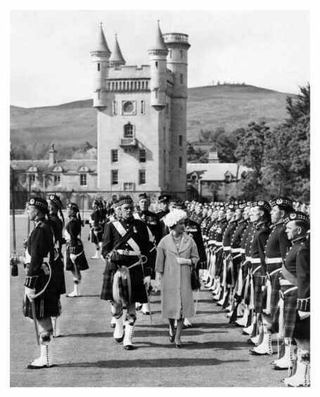 Queen Elizabeth II walks along the front of a crowd of Gordon Highlanders