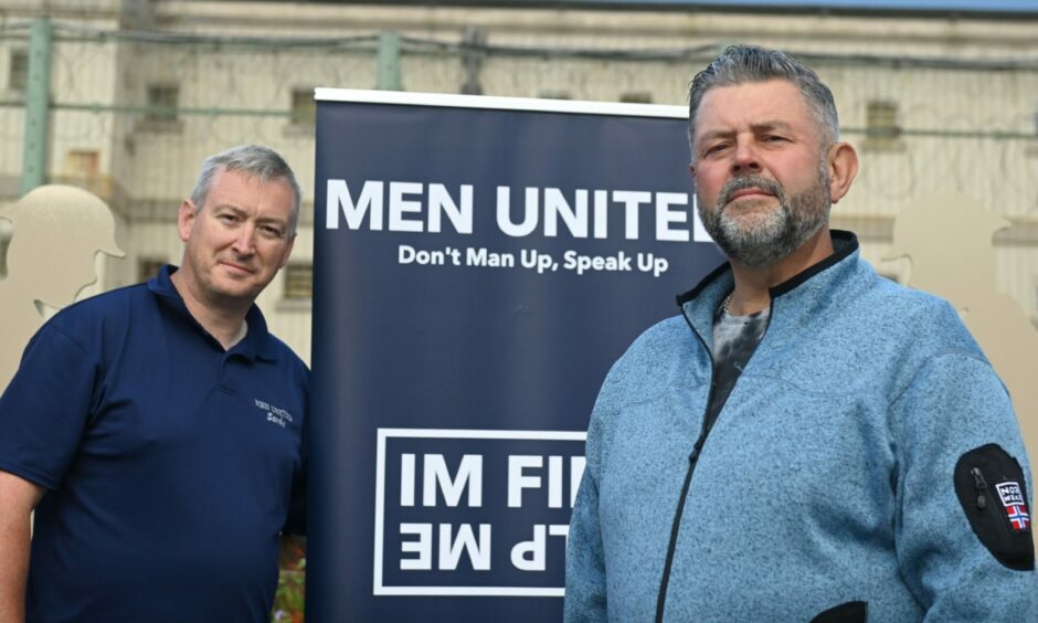 Sandy Garvock standing with Men United chairman Conrad Ritchie in front of a Men United sign.
