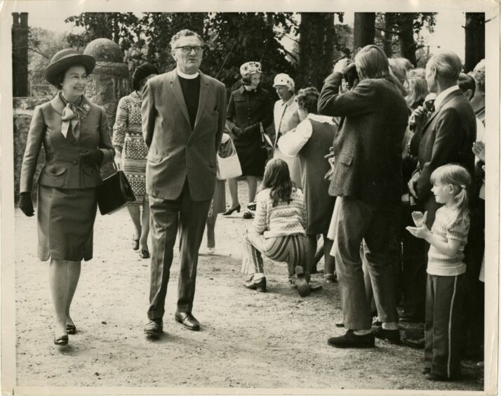 Queen Elizabeth II walking with a minister in front of a crowd of people