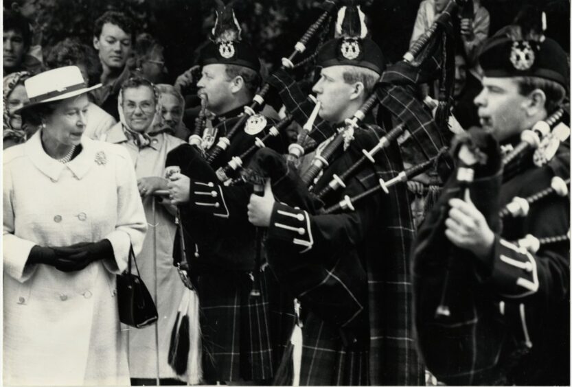 Queen Elizabeth II standing in front of Gordon Highlanders playing the bagpipes