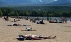 People lying on a beach at Loch Morlich near Aviemore as they enjoy higher temperatures in the north of Scotland.