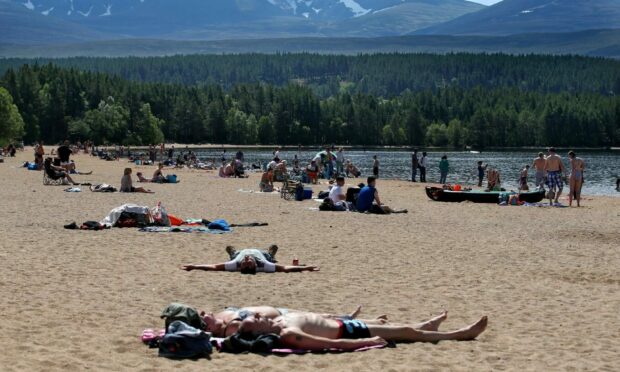 People lying on a beach at Loch Morlich near Aviemore as they enjoy higher temperatures in the north of Scotland.