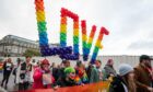 People marching during a pride event, holding up a banner and a balloon that says 'Love'.