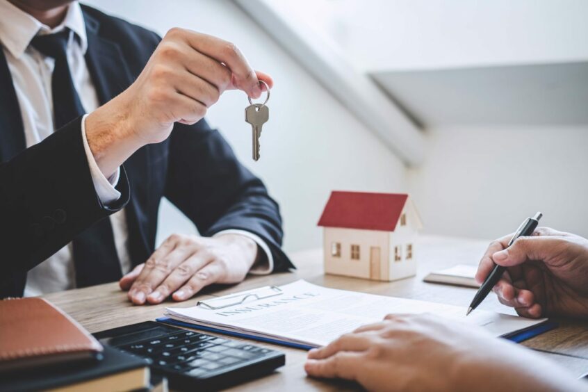 A man hands over house keys to a house buyer signing a contract.