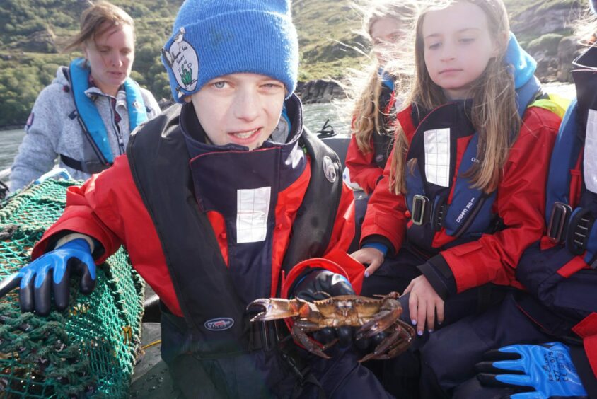 Sea savers on a boat with one of the crabs they caught in a creel.