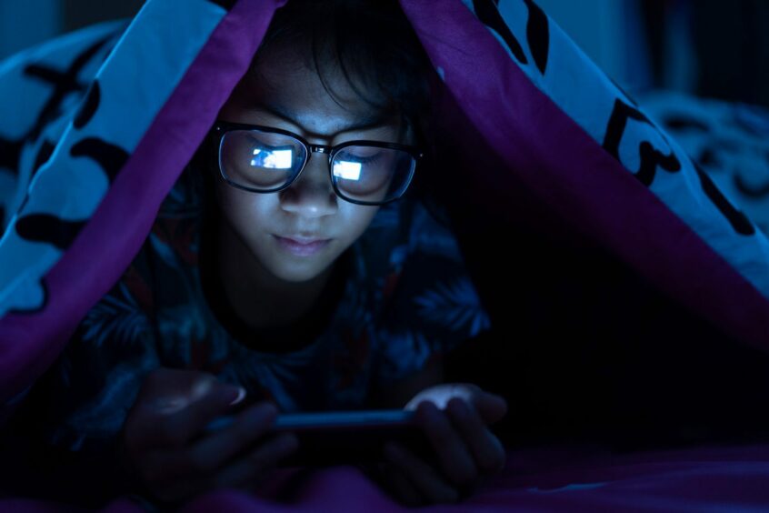 Girl wear blue light glasses using mobile phone on dark bed in the bedroom