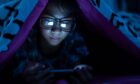 Girl wear blue light glasses using mobile phone on dark bed in the bedroom