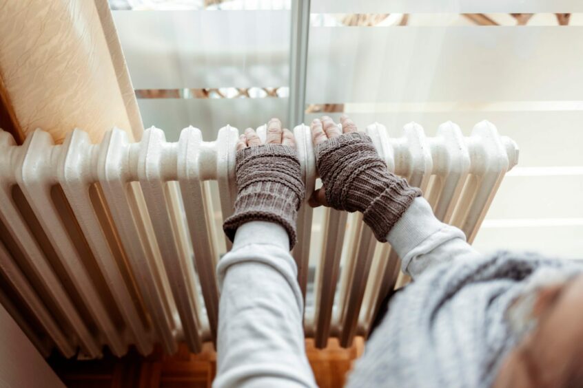 Old men's hands in knitted gloves on heating radiator at home