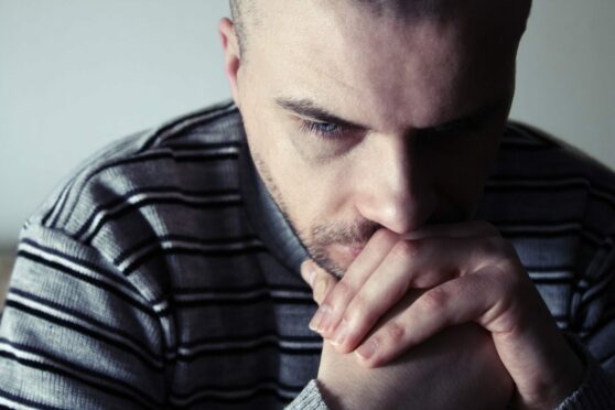 Depressed man holding his hands up to his face and looking deep in thought