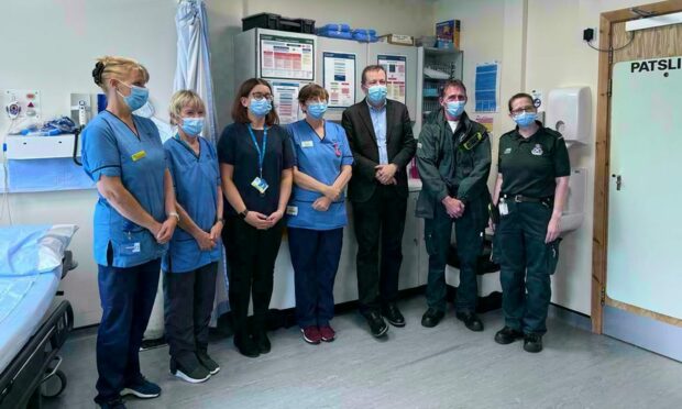 A man in a suit stands in a hospital beside several people in medical scrubs. They are all wearing masks.
