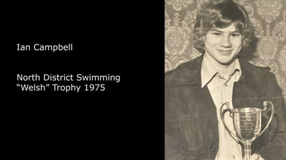 A still from the film. A black screen on the left reads: Ian Campell, North District Swimming "Welsh" Trophy 1975. The black and white photo on the right features a smiling Ian, holding his trophy. 