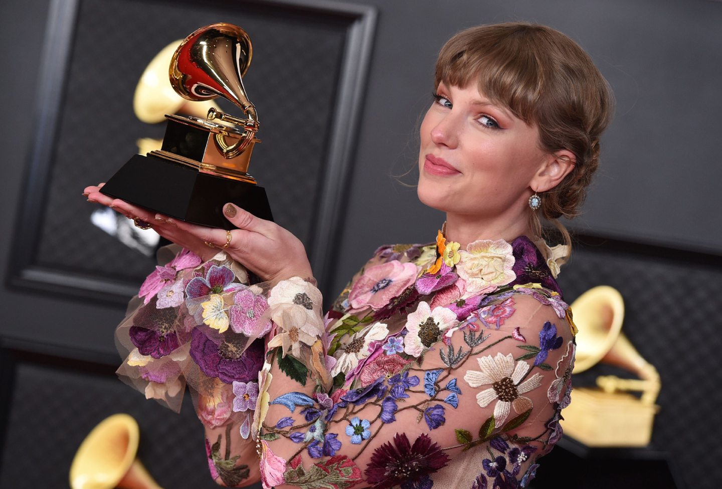 Taylor Swift holding a gold trophy and wearing a flower-patterned dress. 