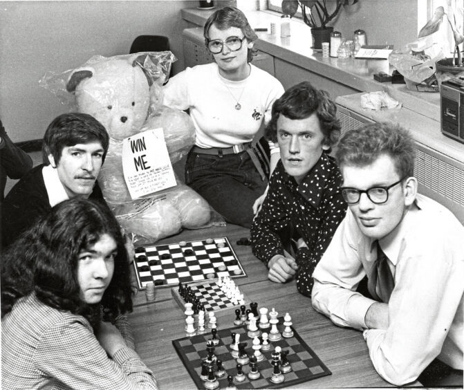 Five staff members sat at a table with a chess board and checkers board. A teddy with a "win me" sign is also on the table.