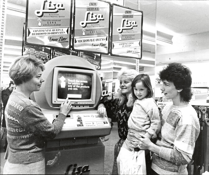 A shop assistant showing three family members a computer in the store.