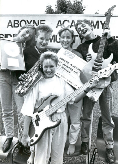 A band holding their instruments along with a giant cheque