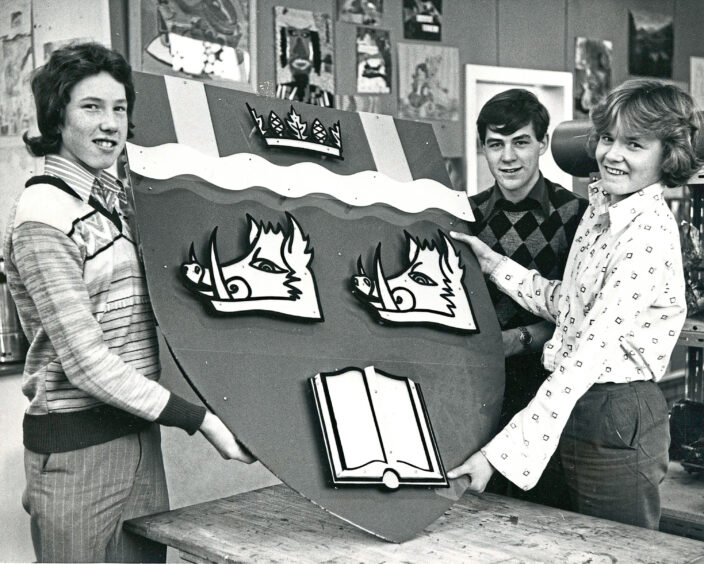 Three pupils hold up the schools coat of arms 