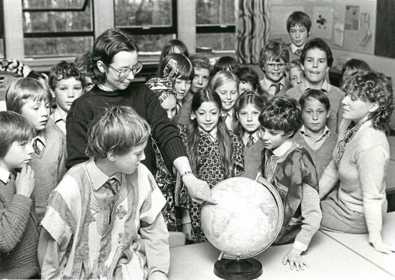 An adult points at a globe in front of a class of pupils at an Aboyne schools