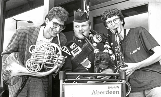 A piper plays pipes in between a French Horn player and a saxophone player at the Aberdeen International Youth Festival
