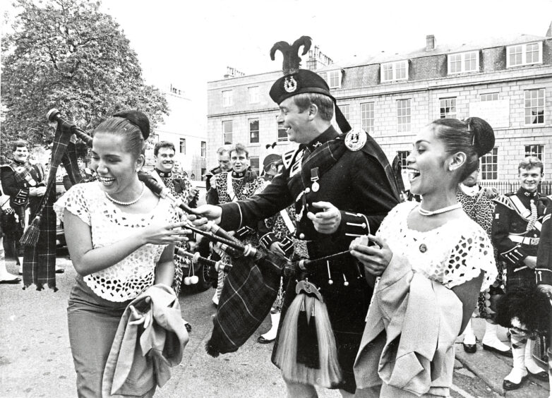 A piper holding out his pipes to girl at the Aberdeen International Youth Festival