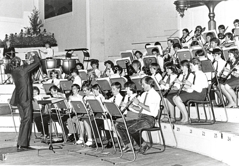 A conductor leading a bans of school children in the Music Hall