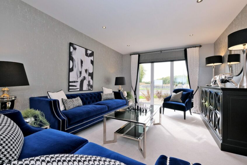 An upscale living room with royal blue velvet couch, large windows, and luxurious fixtures.