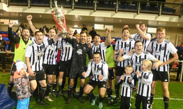 Joe Barbour, centre in black, holds aloft the Evening Express Aberdeenshire Cup after Fraserburgh's penalty shoot-out victory against Formartine United