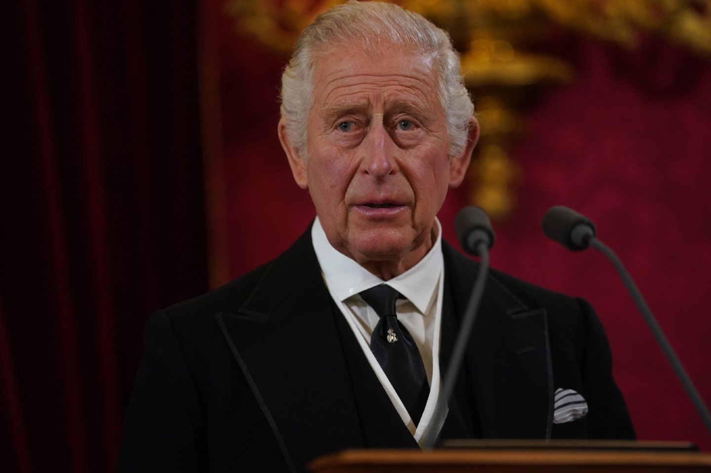King Charles looking solemn while standing at podium giving a speech 