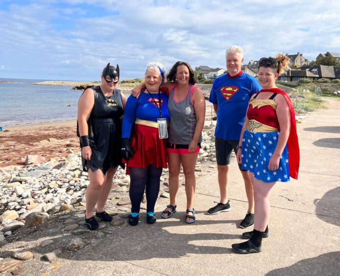 The swimmers in superhero costumes standing with the beach behind them