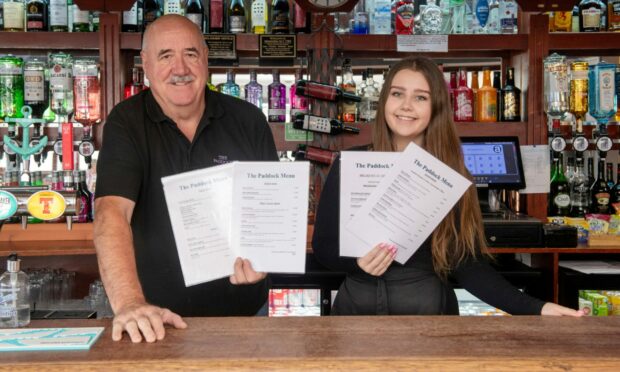 The Paddock owner John Burgess stand behind his bar with staff member Heather Clark. The publican has reduced his menu prices.