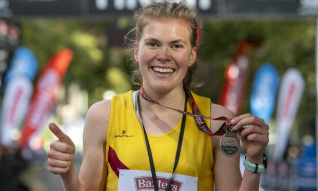 Megan Keith holding a medal up and giving the camera a thumbs up