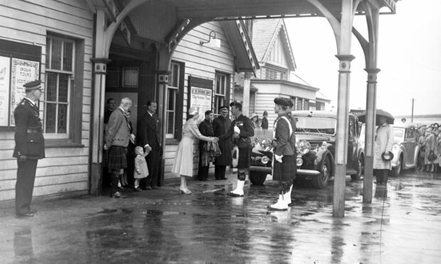 Queen Elizabeth, Prince Philip, Prince Charles, and Princess Anne arriving at Ballater Station in August 1952. Queen Elizabeth is greeted by soldiers at Ballater Station, one holding a sword. Prince Philip stands holding Prince Charle's hand.