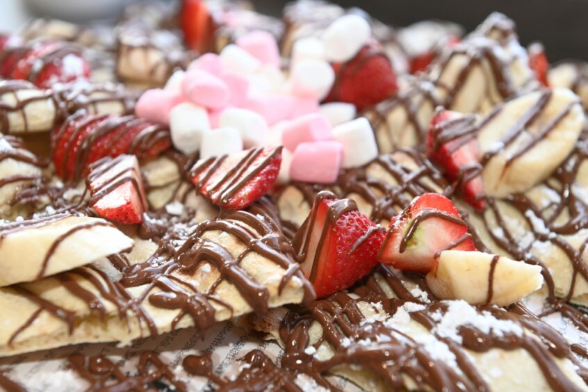 A pizza base covered in nutella, strawberries, banana slices and marshmallows