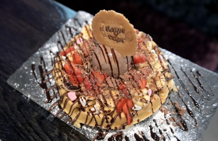 A waffle covered in strawberries, banana, marshmallows, chocolate sauce and ice cream