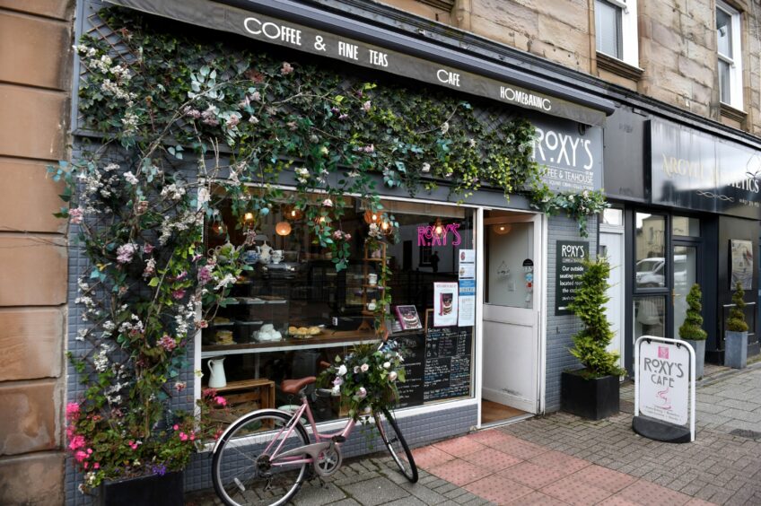The pedestrian crossing at Argyll Square is right next to Roxy's Cafe. Roxy's Cafe has ivy growing along the outside and it has a big window and an old pink bike outside.