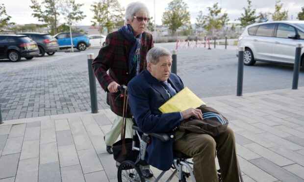 Bill MacDowell in his wheelchair being pushed by his wife Rosemary outside court