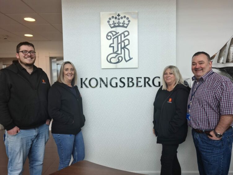 The Kongsberg mental health first aid team standing in front of a sign reading "Kongsberg" with the logo above it