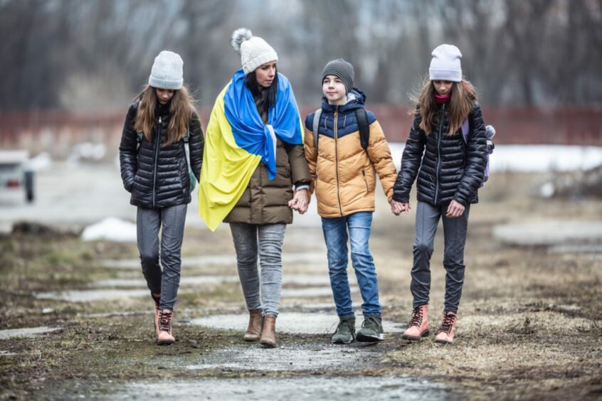 Four people walking in a row, one woman has a Ukraine flag draped around her shoulders