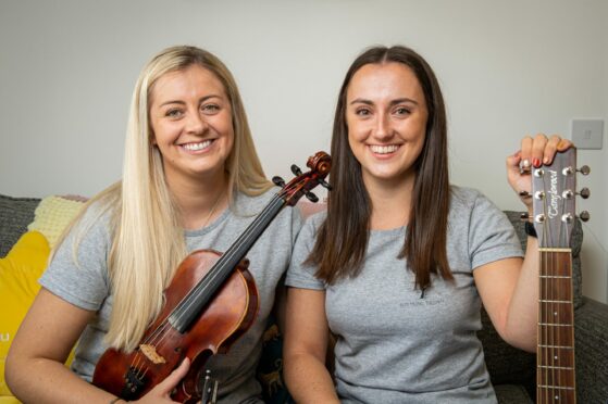 Emmeline McCracken holding her violin next to fellow music therapist Nadine Allan who is holding the end of her guitar